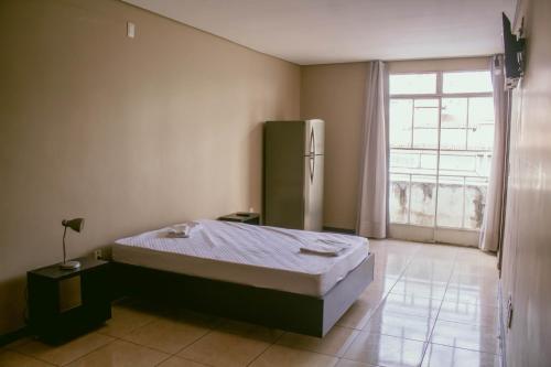 a bedroom with a bed and a refrigerator and a window at Kitnet em Betim no centro in Betim