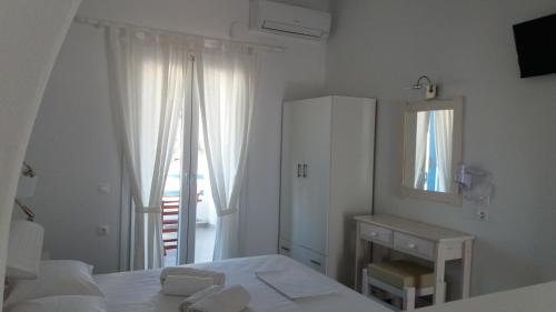 a white bedroom with a bed and a mirror at Taxiarchis Studios in Áyios Yeóryios