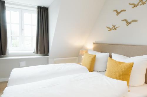 two beds in a bedroom with white sheets and yellow pillows at Stadtrose in Westerland