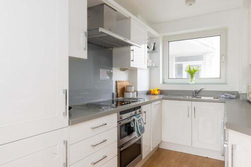 a kitchen with white cabinets and a sink and a window at Sunny & Modern Near the Beach & Village w Parking in East Wittering