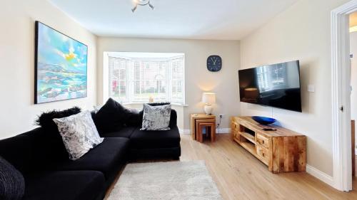 a living room with a black couch and a flat screen tv at Baileys Beach House - Part of the The Bay Filey Holiday Village with pool, gym and direct beach access, pub, restaurant, tennis and meadows walks in Filey