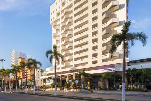 a large white building with palm trees in front of it at Sunvivia by Fiesta Americana Mazatlán in Mazatlán