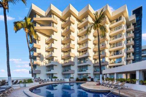 a building with a swimming pool and palm trees at Sunvivia by Fiesta Americana Mazatlán in Mazatlán