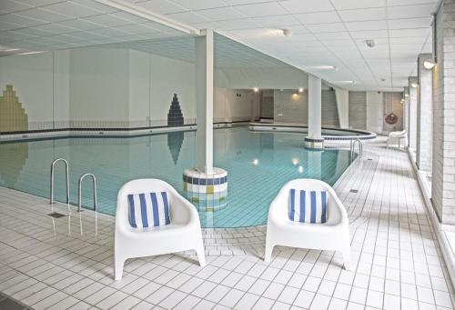una piscina con 2 sillas blancas delante en Fletcher Hotel Restaurant De Eese en De Bult