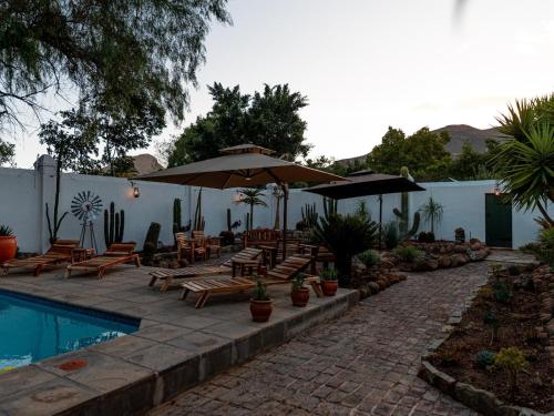 a patio with chairs and umbrellas next to a pool at Far Far Away Guesthouse - 4-star Luxury Karoo Escape with Garden, Pool & Personal Touch in Graaff-Reinet