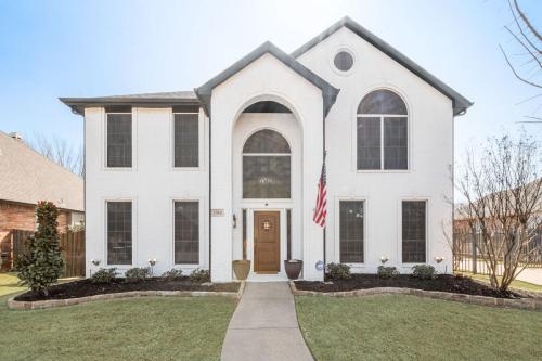 a white house with a flag in the front yard at Elegant 5BR Pool House with Cinema Fire Pit and Games in Keller