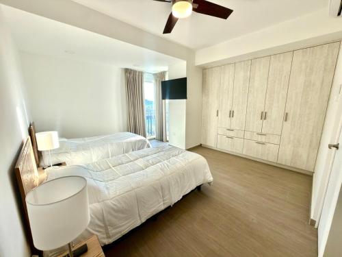 a white bedroom with two beds and a ceiling fan at Spacious Central Apartment, Pool & Gym, Group Friendly in Hermosillo