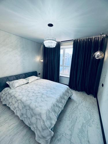 a bedroom with a bed with blue curtains and a chandelier at Перлина Люкс in Khmelnytskyi