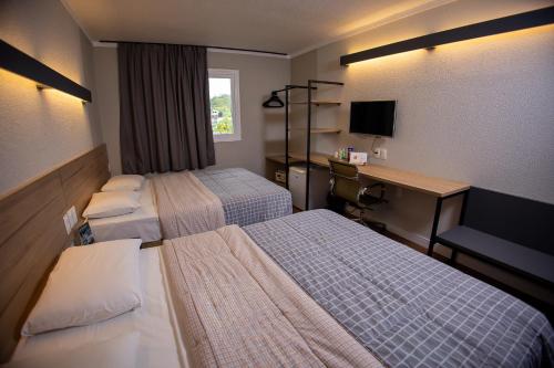 a hotel room with two beds and a desk at Hotel 10 Blumenau in Blumenau