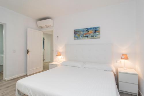 a white bedroom with a white bed and two lamps at Villa Anglesos in Can Picafort