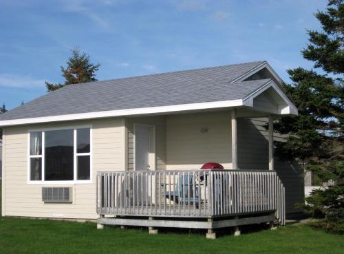 a small white house with a wooden porch at Seascape Coastal Retreat - 2 ADULTS ONLY - HOT TUB AND WITHOUT HOT TUB OCEANFRONT PROPERTY in Ingonish
