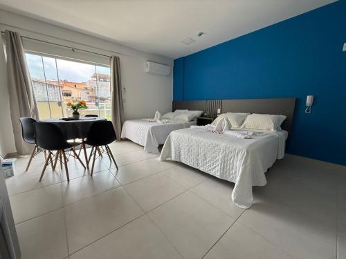 a bedroom with two beds and a table and a blue wall at Condomínio Aparte Hotel Laguna in Arraial do Cabo