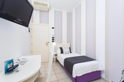 a small room with a bed and a desk and a tv at Hotel Flora in Milano Marittima