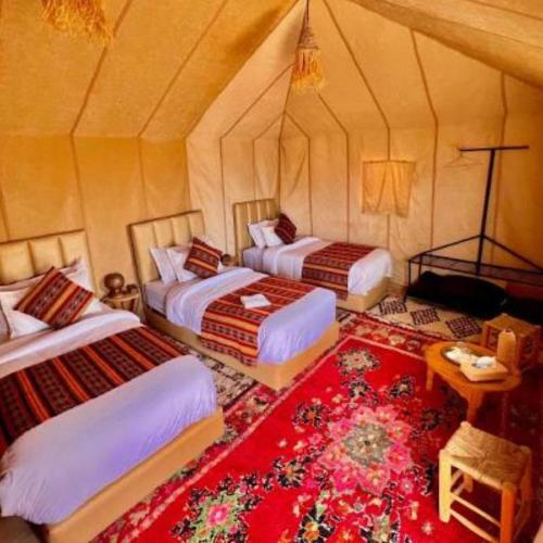 a bedroom with two beds and a red rug at Luxury Desert Central Camp in Merzouga