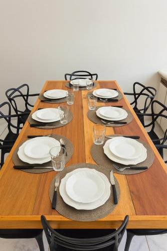 a long wooden table with white plates and glasses at Studio para 7 pessoas com Ar Condicionado e 2 Garagem in Uberlândia