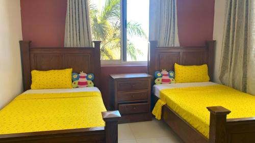 a bedroom with two beds with yellow sheets and a window at Oceanfront Executive Serviced Apartment Mbezi Beach in Dar es Salaam