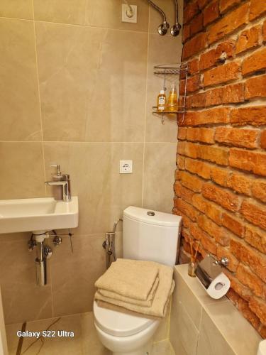 a bathroom with a white toilet and a brick wall at Kaunas Studios - RentA 18 in Kaunas