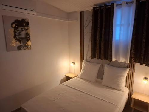 a bedroom with a bed with white sheets and a window at Le Chalet d'Ajoupa in LʼAjoupa-Bouillon
