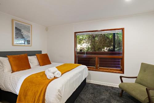 a bedroom with a bed and a window and a chair at The Black Chalet in Whitianga