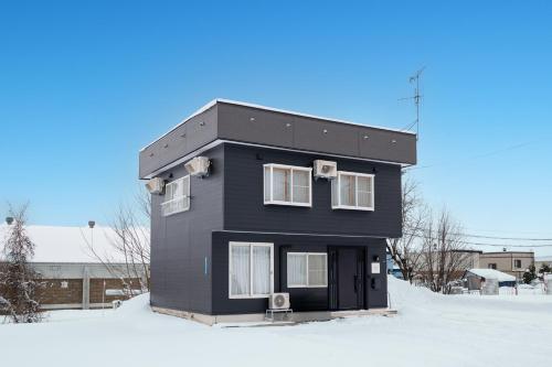 a black house with white windows in the snow at Villa Shigin in Nakafurano
