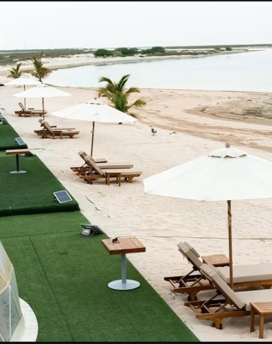 a beach with tables and chairs and umbrellas at Siniya Island Leisure Campground Umm Al Quwain in Umm Al Quwain