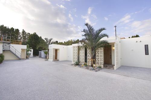 a white building with a palm tree in the driveway at Bise SMC Village in Motobu
