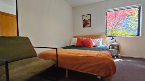 a bedroom with a bed and a chair and a window at Kōwhai Corner Room at Goldfield Heights in Queenstown