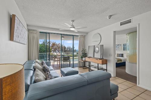 a living room with a blue couch and a television at Grand Palais Boolarong Beachside Apartments in Alexandra Headland
