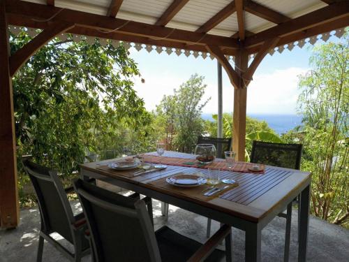 a wooden table with chairs on a patio with a view at Ti Sucrier Jaune - Douceur caraïbe vue mer in Le Carbet