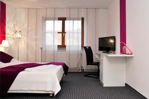 Habitación de hotel con cama, escritorio y TV. en Hotel zum Brunnen en Friedberg