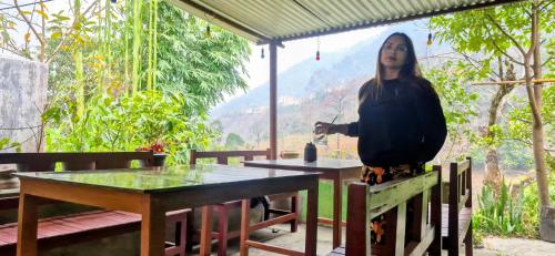 a woman is standing in front of a table at Riverside hostel in Ghanpokhara