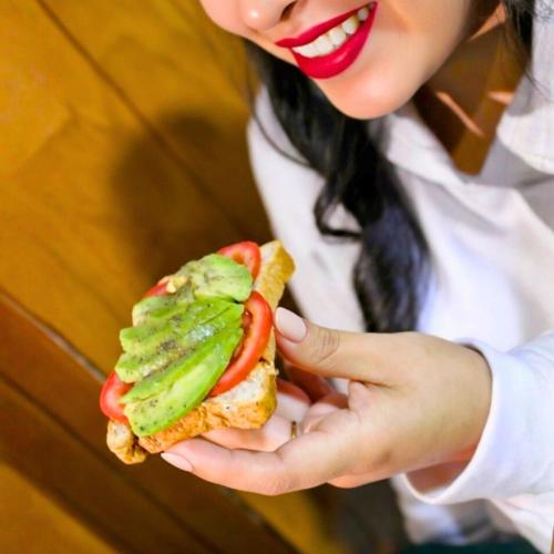a woman is holding a sandwich with avocado and tomatoes at Lua Hostal - Arequipa in Arequipa