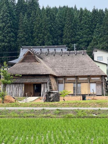an old house with a straw roof in a field at うご八かやぶ㐂 in Narazaki