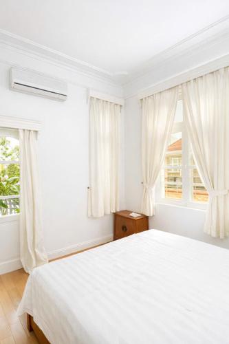 a white bedroom with a bed and two windows at Davidduc Villa 30 Tay Ho in Hanoi