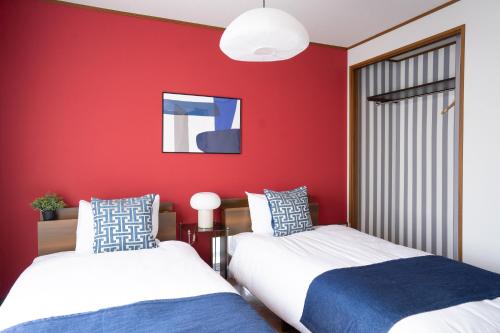 two beds in a room with a red wall at cozy 3rd stay in Okayama