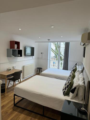 a bedroom with two beds and a table and a desk at Berjaya Eden Park London Hotel in London