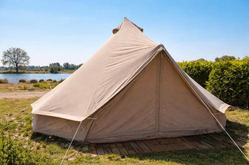 a canvas tent in the grass next to a lake at Bell Tent aan de haven in Heerewaarden