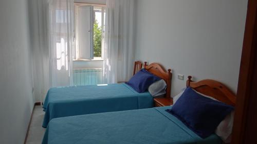 a bedroom with two beds with blue sheets and a window at Casa Bruna 1º A Apartamento a 800 m de la playa in Lariño