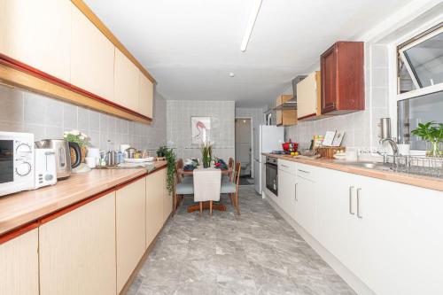 a kitchen with white cabinets and a table in it at Xtra Large 4 Bedroom House with Heating Sleeps 14 Near Station and ExCeL in London