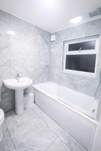 a white bathroom with a sink and a tub and a toilet at Xtra Large 4 Bedroom House with Heating Sleeps 14 Near Station and ExCeL in London
