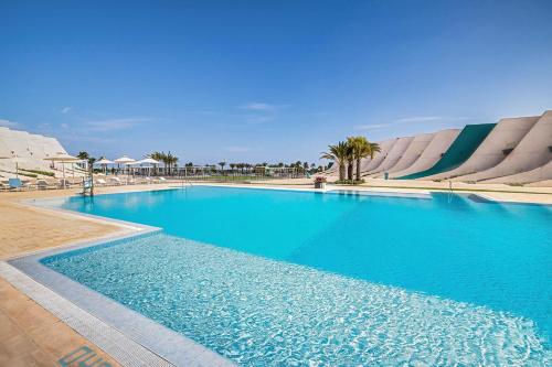 a large blue swimming pool with palm trees and buildings at Occidental Mar Menor in Cartagena