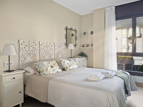 a white bedroom with a large bed with a window at Apartamento en la playa con piscina - Azcona 6004 in Noja