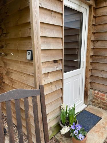 a wooden house with a door and a chair and flowers at Mustard Pot Cottage in Eye