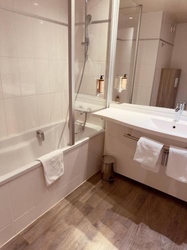 a white bathroom with a tub and a sink at Mercure Rouen Val de Reuil in Val de Reuil