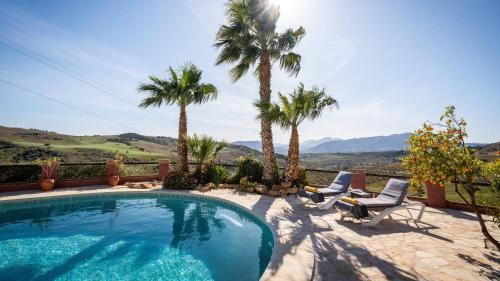 a swimming pool with two chairs and palm trees at Finca Gran Cerros in Alora