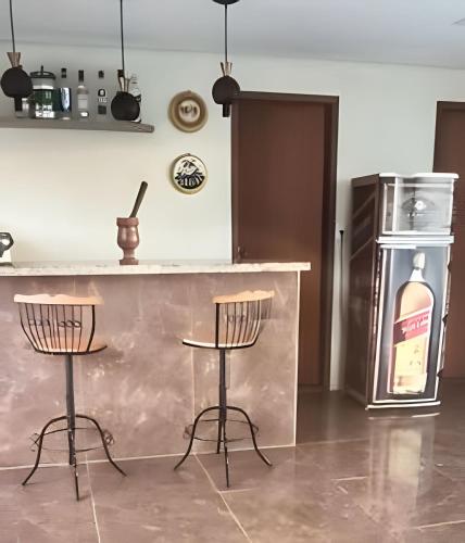 a kitchen with a bar with two chairs and a refrigerator at Cobertura com piscina, sauna e churrasqueira in São Pedro da Aldeia