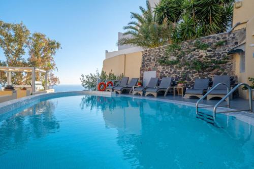 a swimming pool with chairs and the ocean in the background at Ersi Villas in Firostefani