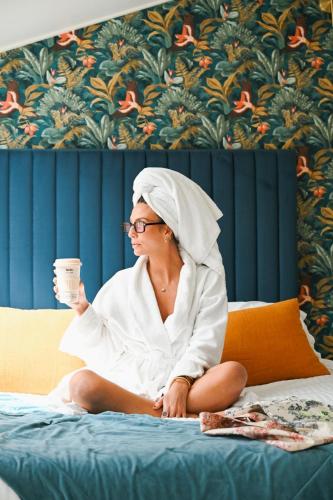 a woman sitting on a bed holding a cup of coffee at Hôtel & Suites San Roccu in Saint-Florent