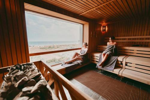 two women sitting on benches in a room with a window at Bauernhaus 3 -Vaest- in Fehmarn
