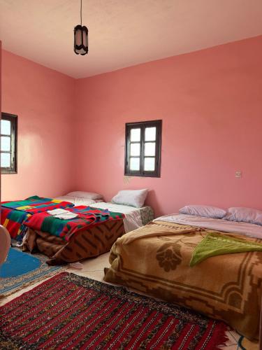 two beds in a room with pink walls at Maison La Baraka Merzouga in Merzouga